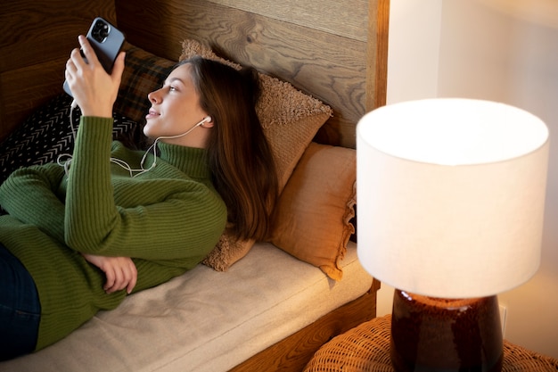 Free photo woman searching for something on the internet using her smartphone while laying on her bed