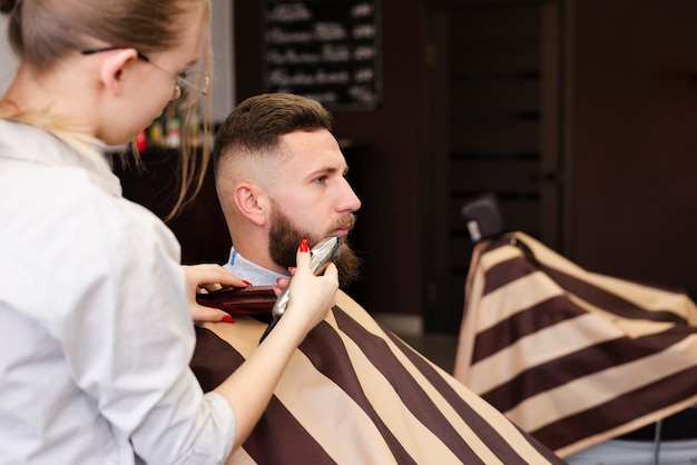 Woman shaving her client's beard with copy space