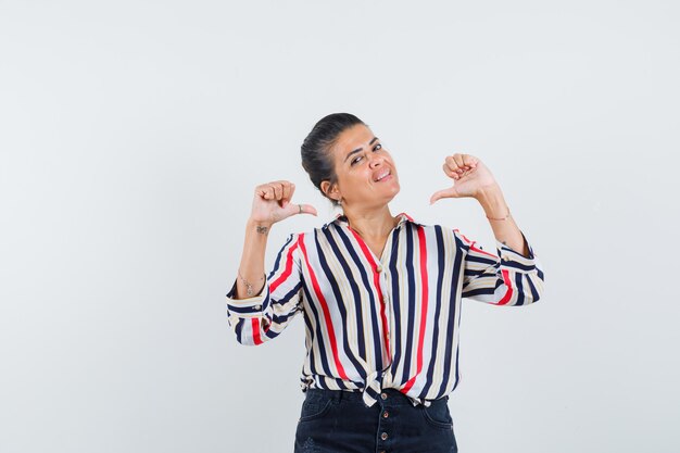 woman in shirt, skirt pointing at herself with thumbs and looking proud