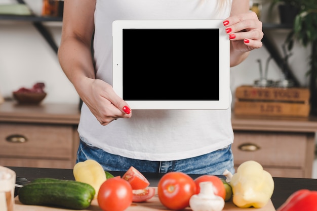 Free photo woman showing blank digital tablet standing behind the vegetables on table