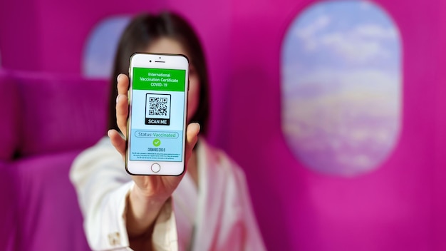 Woman showing COVID19 International Vaccination Certificate with QR code on a phone pink background