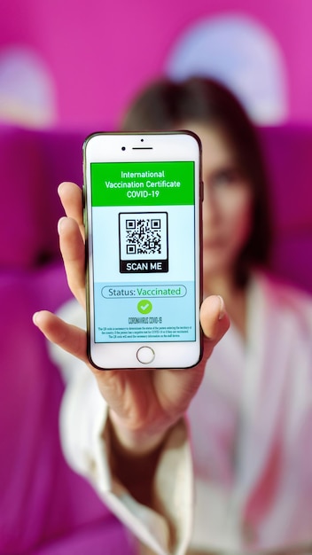 Woman showing COVID19 International Vaccination Certificate with QR code on a phone pink background