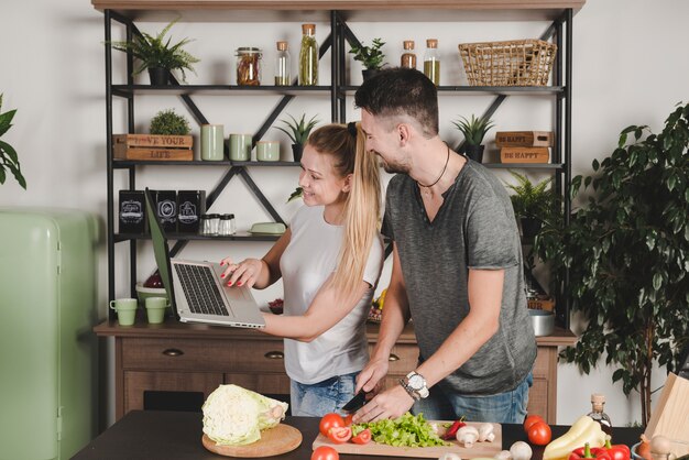 Woman showing laptop to her husband cutting vegetables in the kitchen