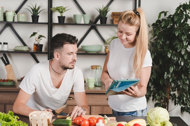 Free photo woman showing laptop to man cutting vegetables