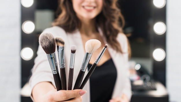 Woman showing makeup brushes on mirror background