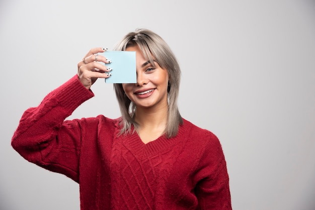 Woman showing memo pad on gray background.