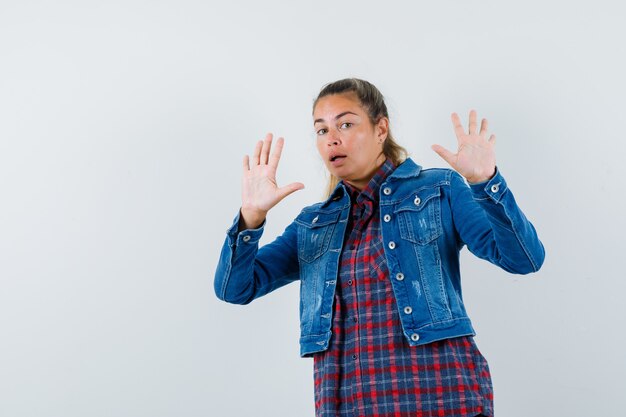 Woman showing palms in surrender gesture in shirt, jacket and looking scared. front view.