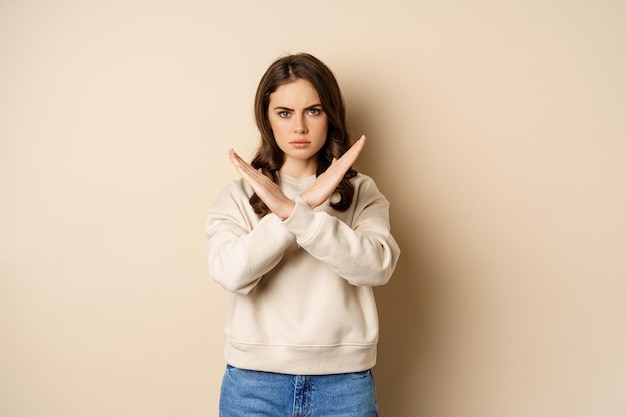 Woman showing stop cross sign gesture and frowning angry dislike and disapprove saying no rejecting ...