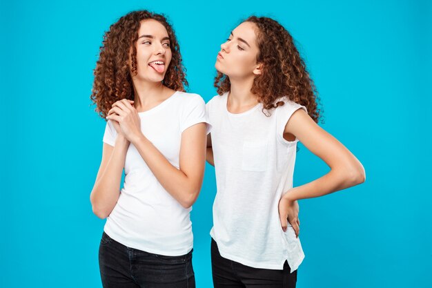 woman showing tongue her sister twin over blue wall