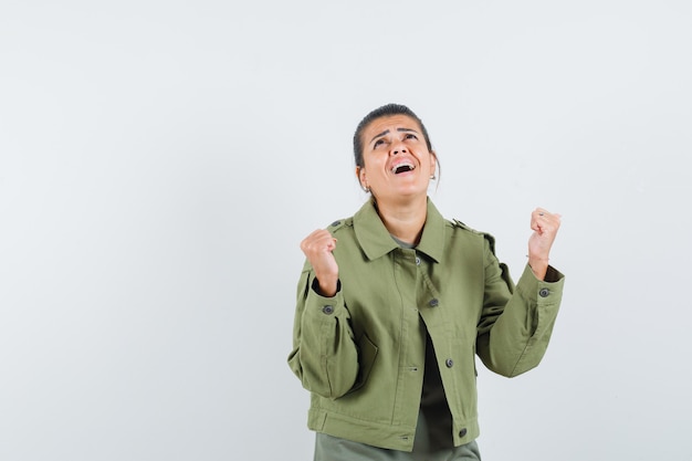 woman showing winner gesture in jacket, t-shirt and looking happy