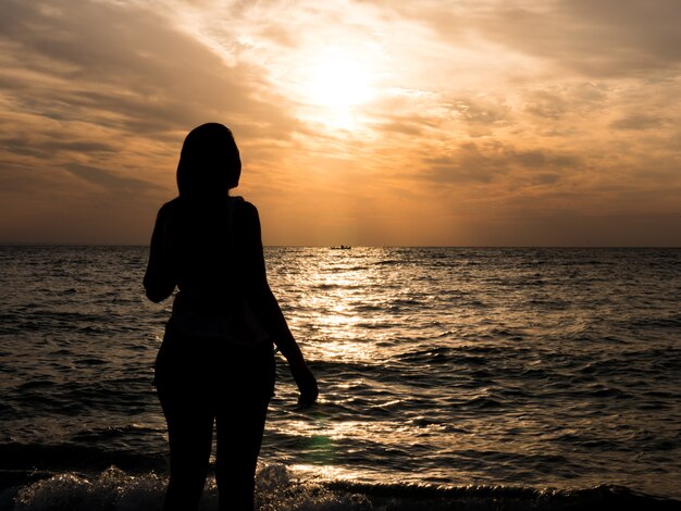 Woman silhouette watching sun on the beach at sunset.. Tourist girl on beach holiday