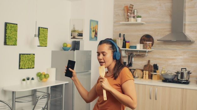 Free photo woman singing in the morning using wooden spoon. energetic, positive, happy, funny and cute housewife dancing alone in the house. entertainment and leiuse alone at home