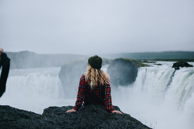 Woman sit on edge of cliff on waterfall