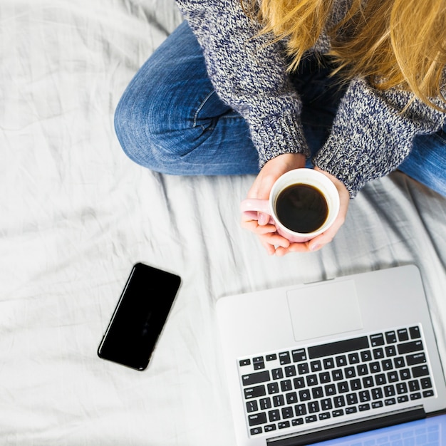 Woman sitting on bed with laptop and coffee 