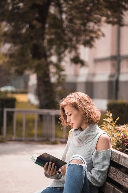 Free photo woman sitting on bench and reading book in park