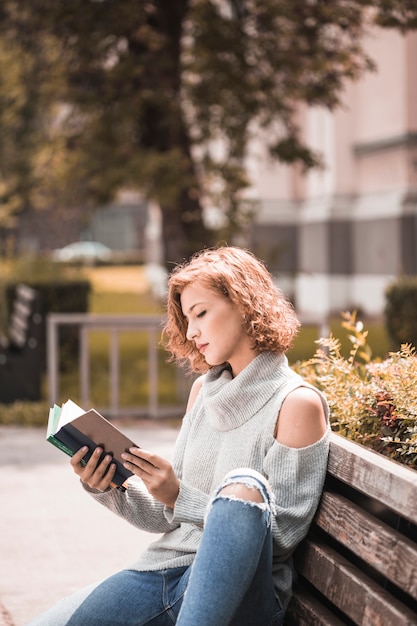 Free photo woman sitting on bench and reciting volume in park