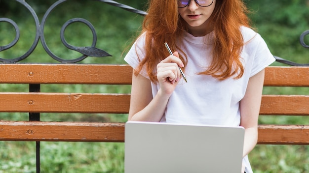 Woman sitting on bench with laptop and pen 