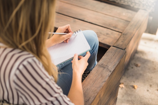 Free Photo woman sitting on bench writing over notebook with pencil