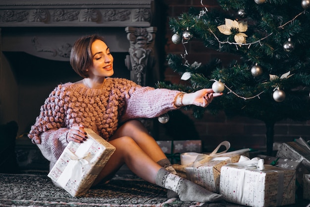 Woman sitting by Christmas tree surrounded with presents