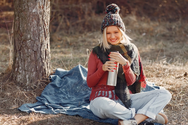 Free photo woman sitting by a tree in a spring forest with a drink thermos