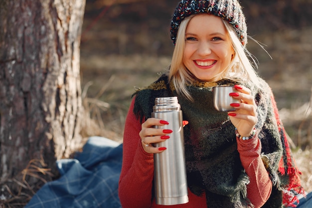 Free photo woman sitting by a tree in a spring forest with a drink thermos