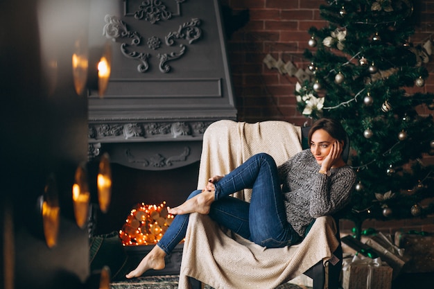 Woman sitting in chair by Christmas tree