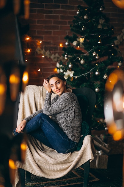 Woman sitting in chair by Christmas tree