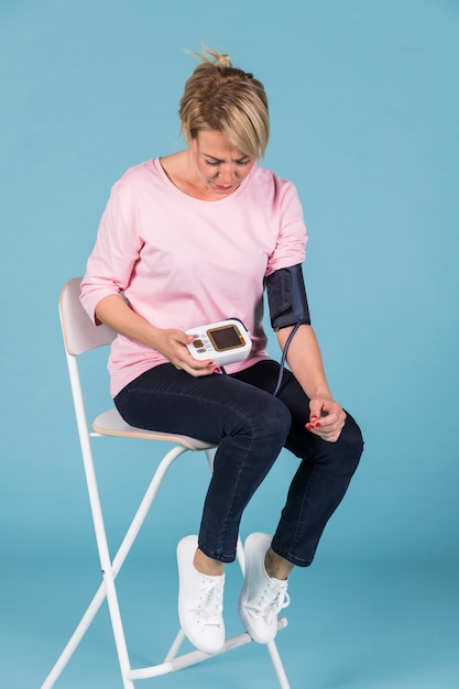 Woman sitting on chair checking blood pressure on electric tonometer