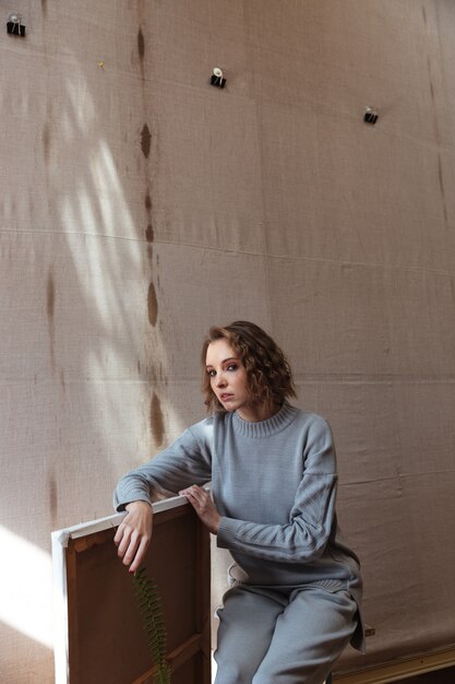 Free photo woman sitting on a chair and leaning against a canvas