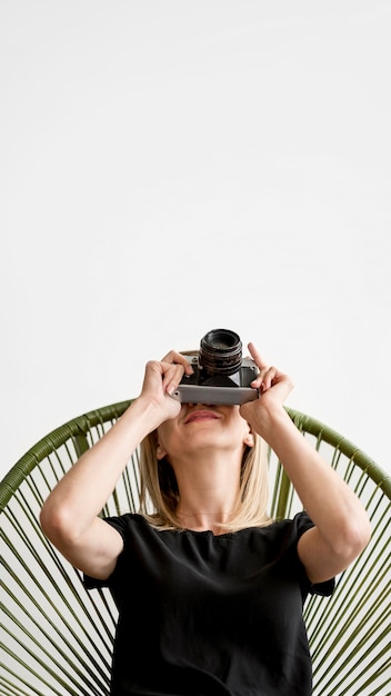 Free photo woman sitting on a chair and taking a picture