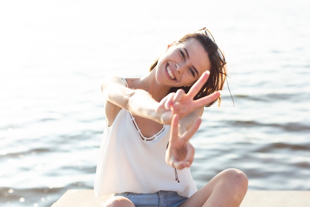 Free Photo woman sitting on dock doing the peace sign