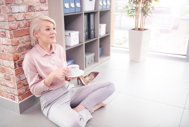 Free photo woman sitting on floor with cup of coffee at office