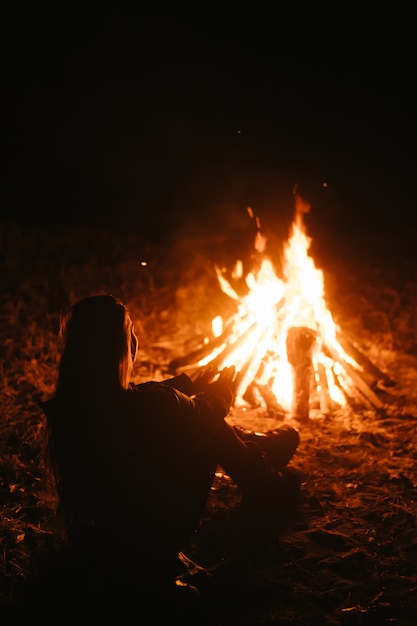 Free Photo woman sitting and getting warm near the bonfire in the night forest