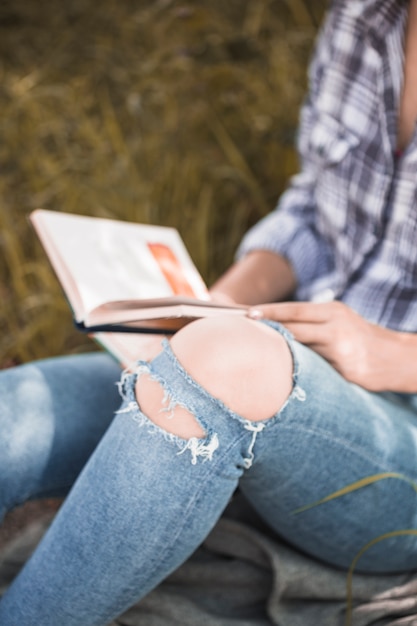 Free photo woman sitting on grass with book in distressed jeans