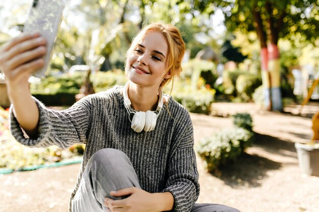 woman sitting in greenhouse takes selfie on her phone