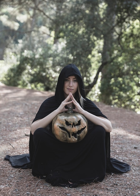 Free Photo woman sitting on ground and holding pumpkin in park