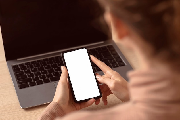 Free Photo woman sitting next to her laptop and using smartphone