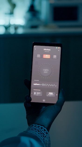 Woman sitting in house with automation light system holding smartphone turning on light using voice activated application