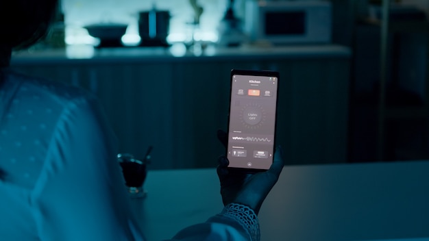 Woman sitting in house with automation light system holding smartphone