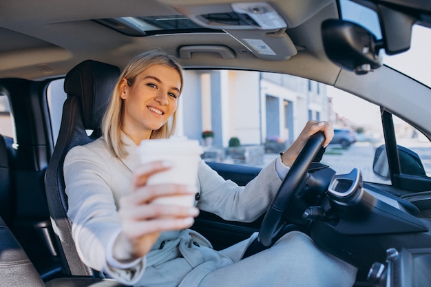 Woman sitting inside electro car while charging with a coffee cup