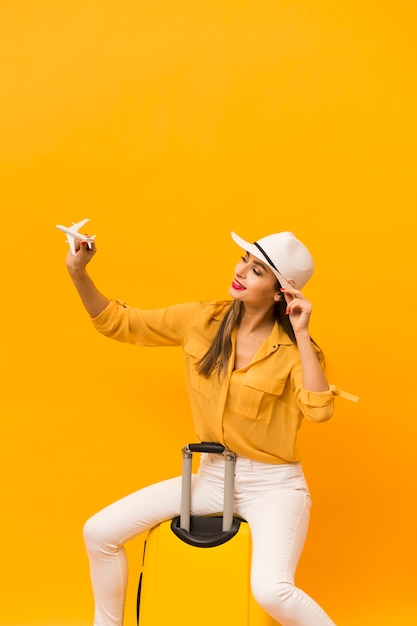 Free photo woman sitting on luggage and holding plane figurine