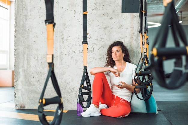 Free photo woman sitting near fitness strap listening to music on mobile phone