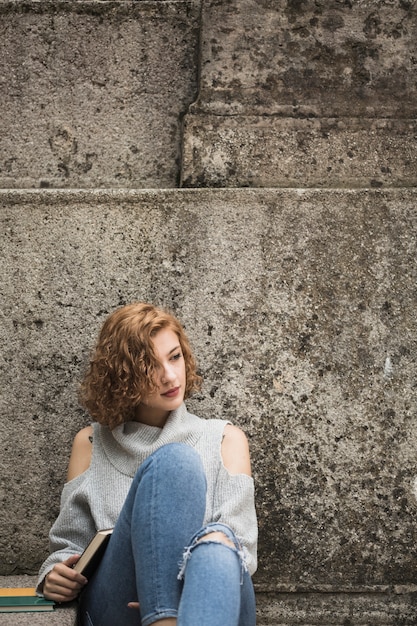 Free photo woman sitting near stone wall