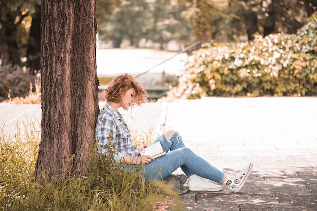 Free photo woman sitting near tree and reading book