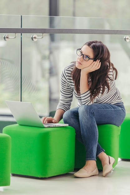 Woman sitting on pouf and using laptop