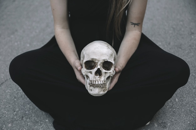 Free photo woman sitting on road holding decorative skull of man between knees