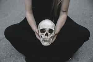 Free photo woman sitting on road holding decorative skull of man between knees