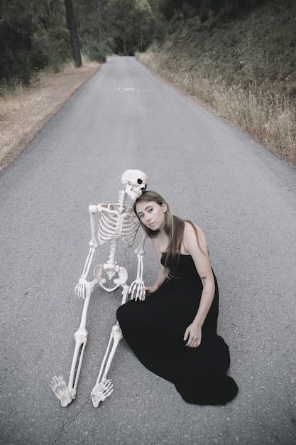 Free photo woman sitting on road with decorative skeleton of man