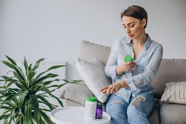 Woman sitting on sofa and holding pills vitamins