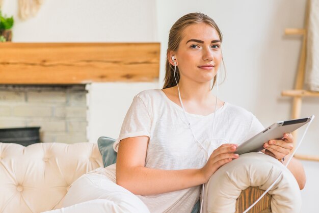 Woman sitting on sofa listening music on earphone through digital tablet